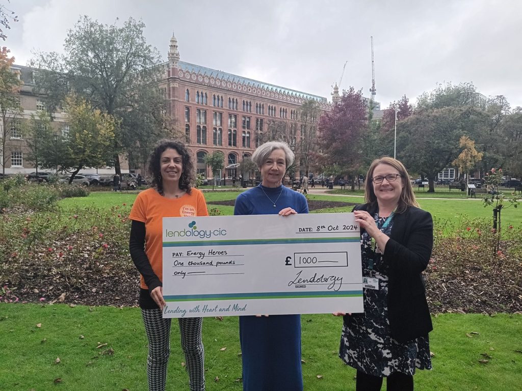 Emma Lower and 2 charity workers for Energy Heroes holing a big cheque, stood in some public gardens