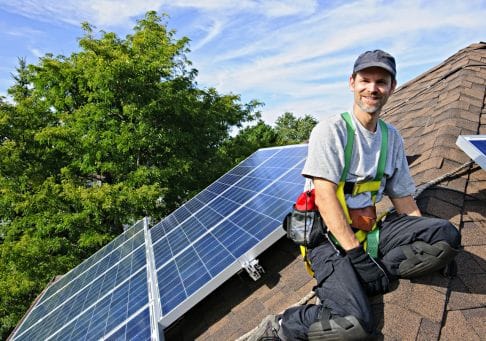 smiling solar panel installer siting on a sloped tile roof