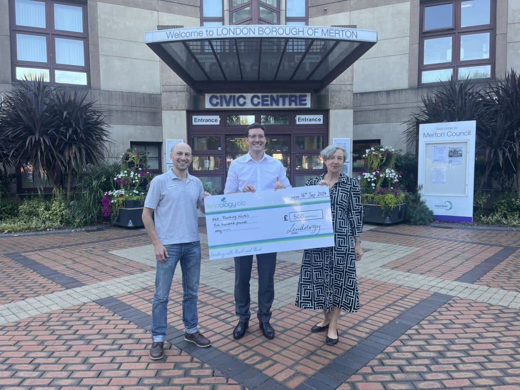 Thinking Works employees and Emma Lower holding a large cheque outside the Civic Centre in Merton