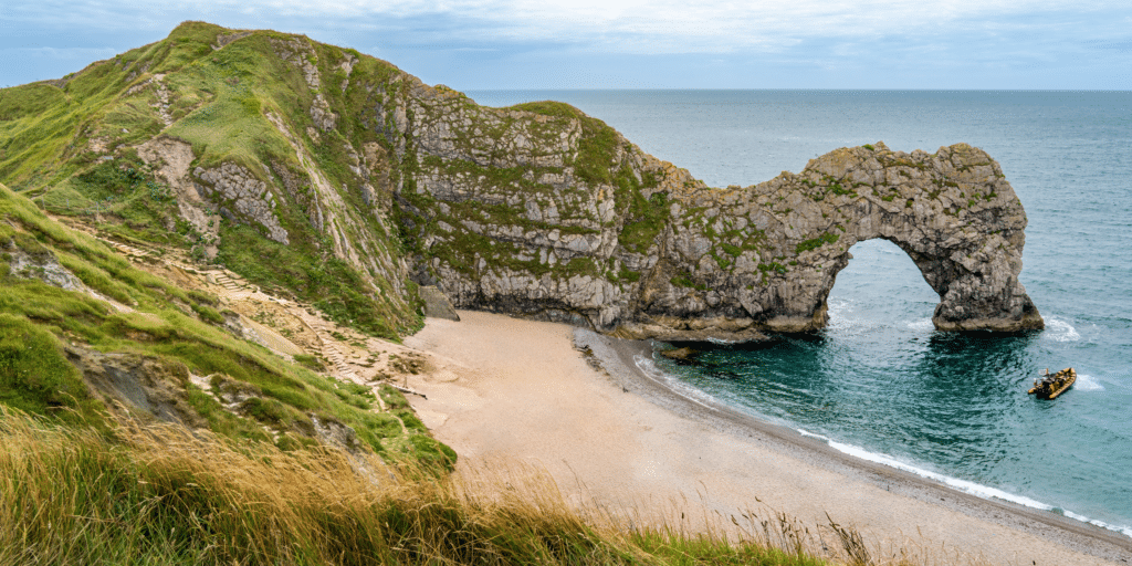 Durdle Door in Dorset, England, with dramatic limestone cliffs, sandy beach and turquoise sea, showcasing the iconic Jurassic Coast landscape on a bright day.