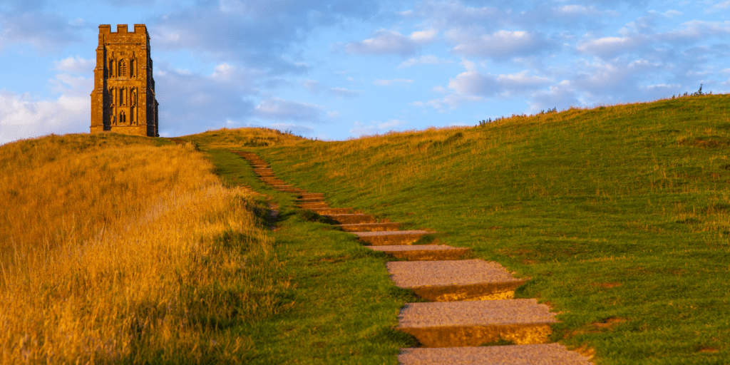 Glastonbury Tor in Somerset at sunset, with the iconic St Michael’s Tower overlooking rolling green hills and a winding footpath in the South West of England.
