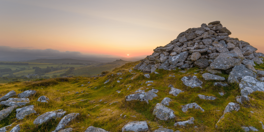 Sunset over Dartmoor National Park in Devon, with rugged moorland, ancient stone cairn and sweeping countryside views across the South West of England.