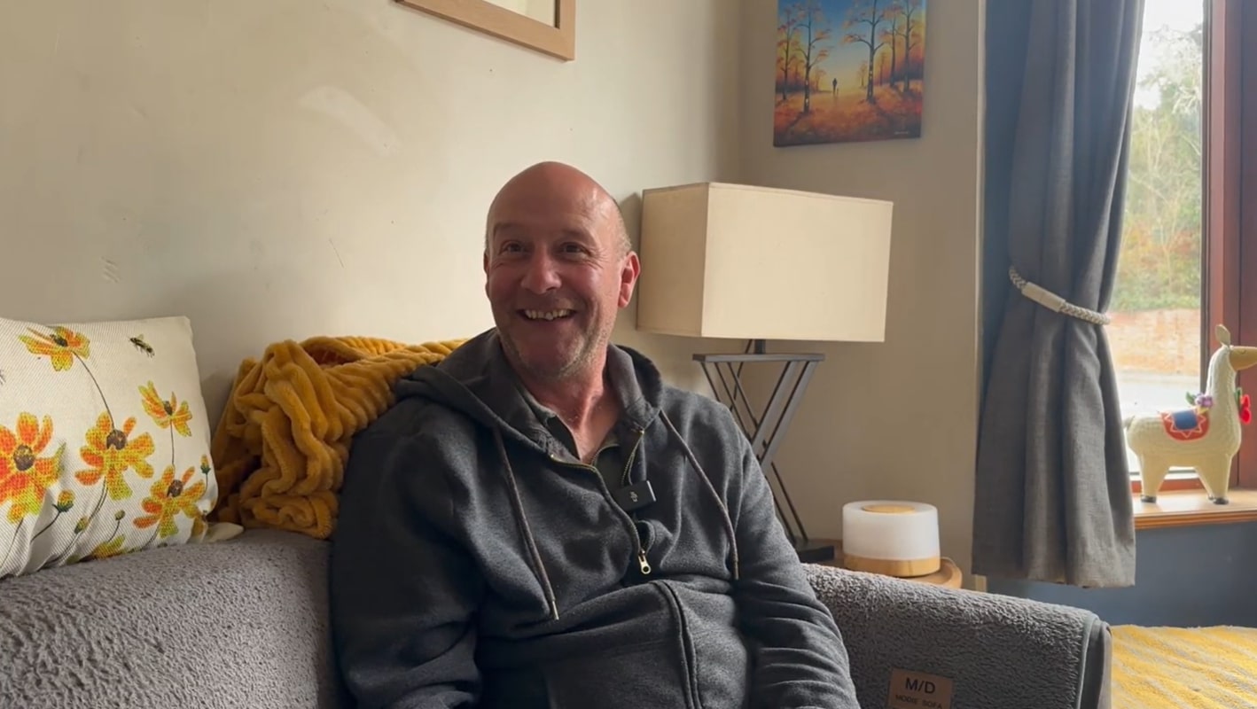 smiling middle-aged man sat on his sofa