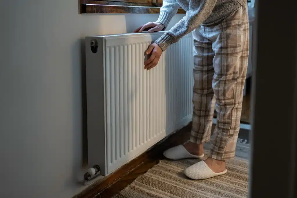 Closeup of woman warming her hands on the heater at home during cold winter days.