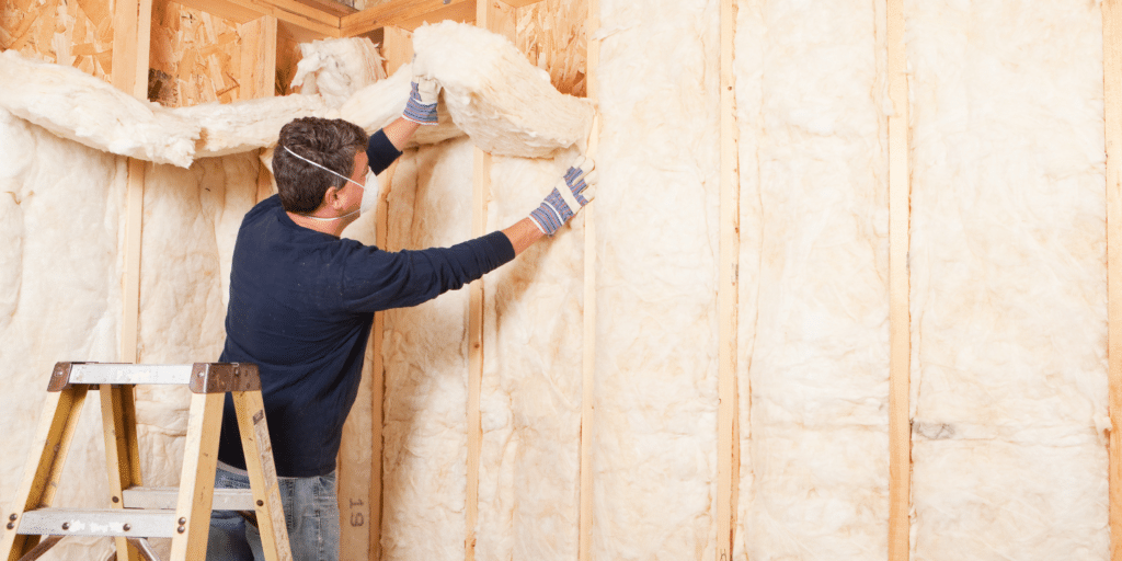 a man installing wall insulation between the battens of an open wall