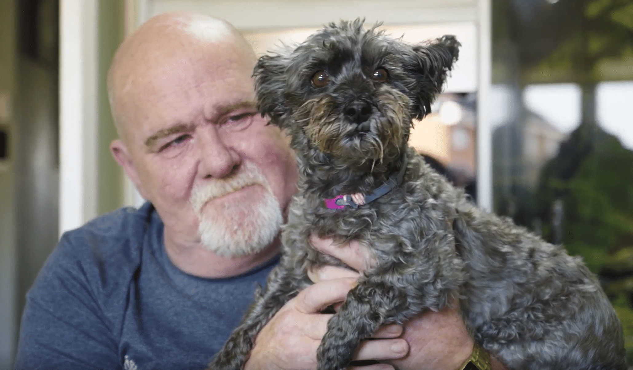 Mark holding his small dog up to the camera and smiling