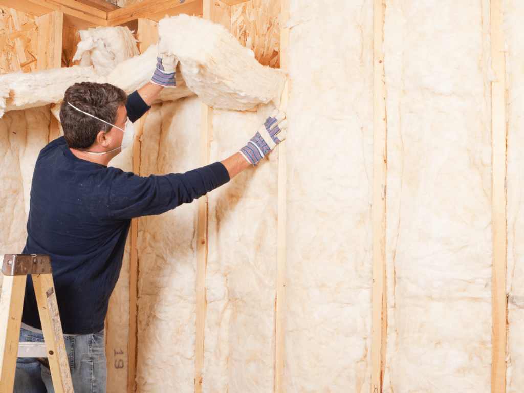 Man fitting fluffy insulation strips between wall cavities