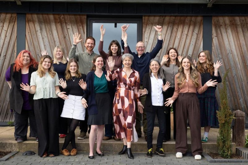 Team members posed for a group photo, smiling and waving at the camera