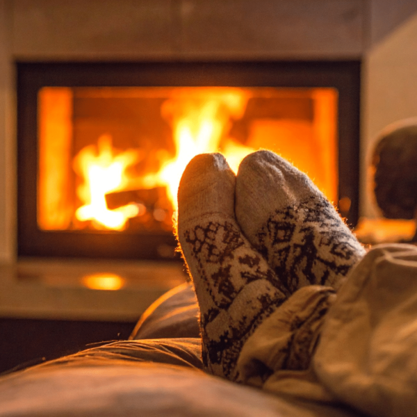 Person relaxing on a sofa with woollen socks, feet up in front of a glowing fireplace, creating a warm and cosy home atmosphere