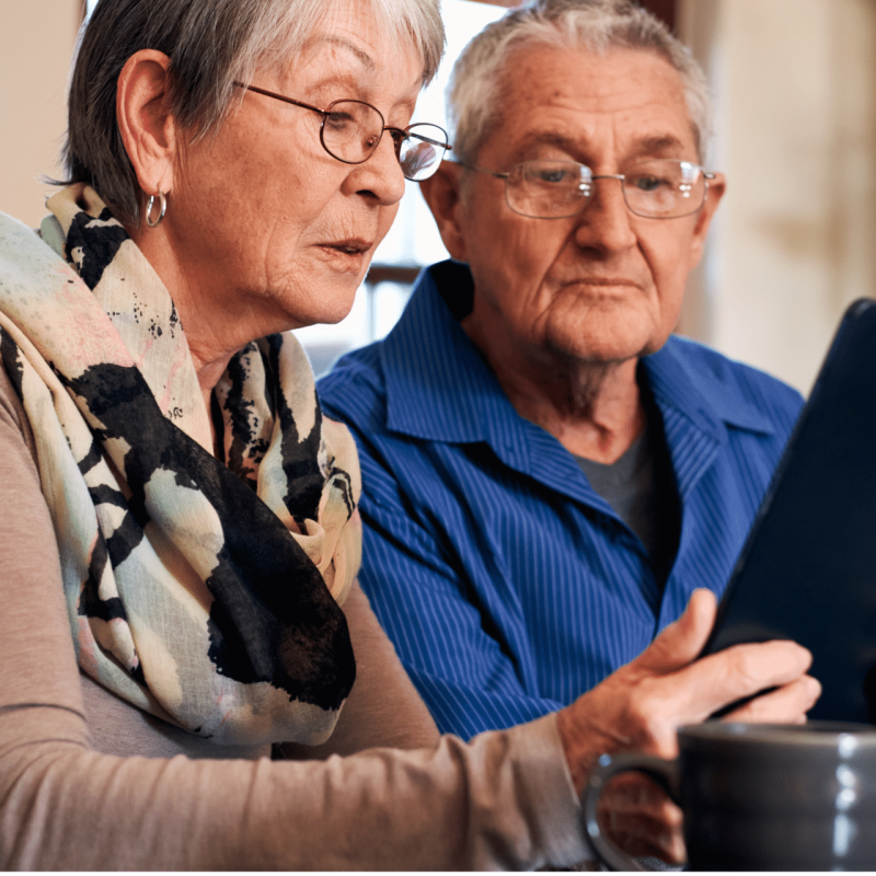 Older couple sitting at a table using a tablet together at home, reflecting digital access, online services and staying connected in later life.