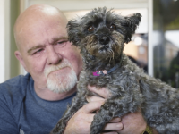 Mark holding his small dog up to the camera and smiling