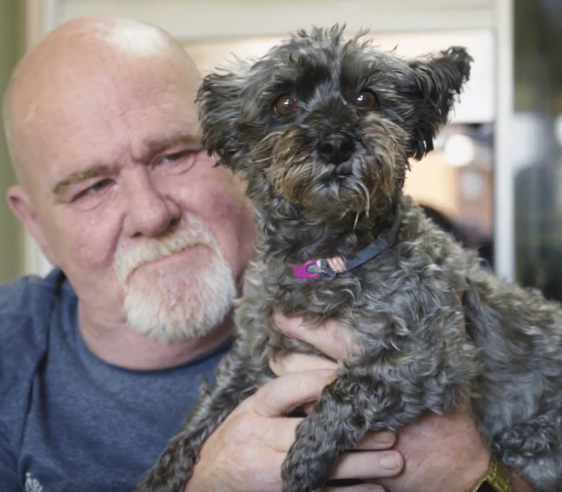 Mark holding his small dog up to the camera and smiling