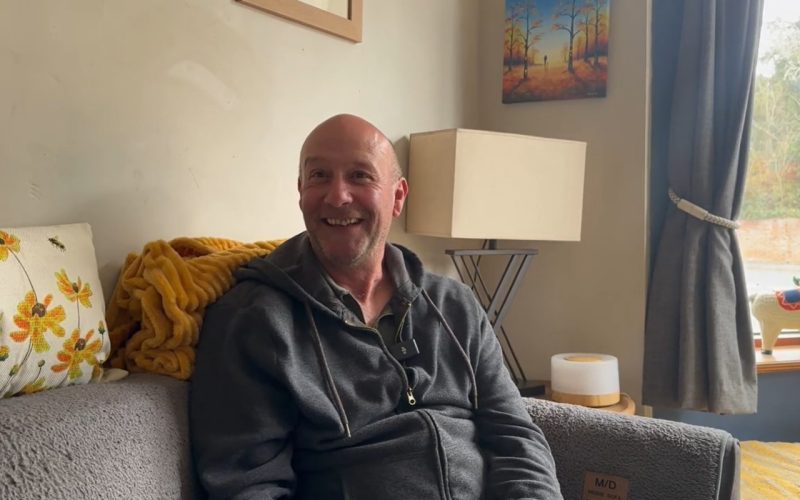 smiling middle-aged man sat on his sofa