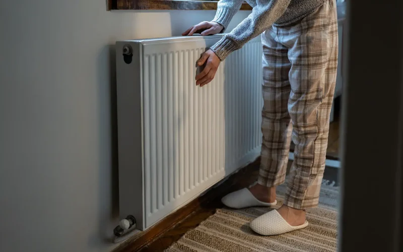 Closeup of woman warming her hands on the heater at home during cold winter days.
